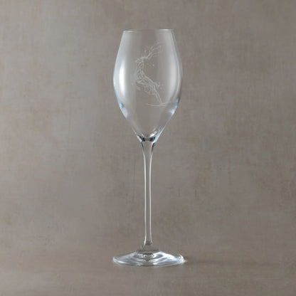Clear prosecco glass engraved with a leaping stag beneath scattered stars, photographed on a soft neutral beige background
