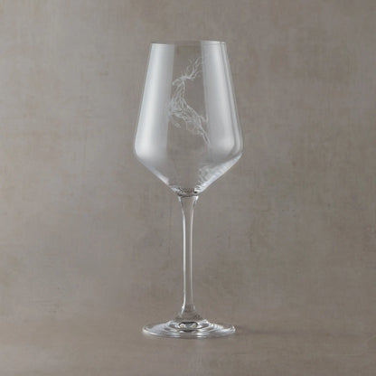 Clear wine glass engraved with a stag and scattered stars on a soft neutral beige background