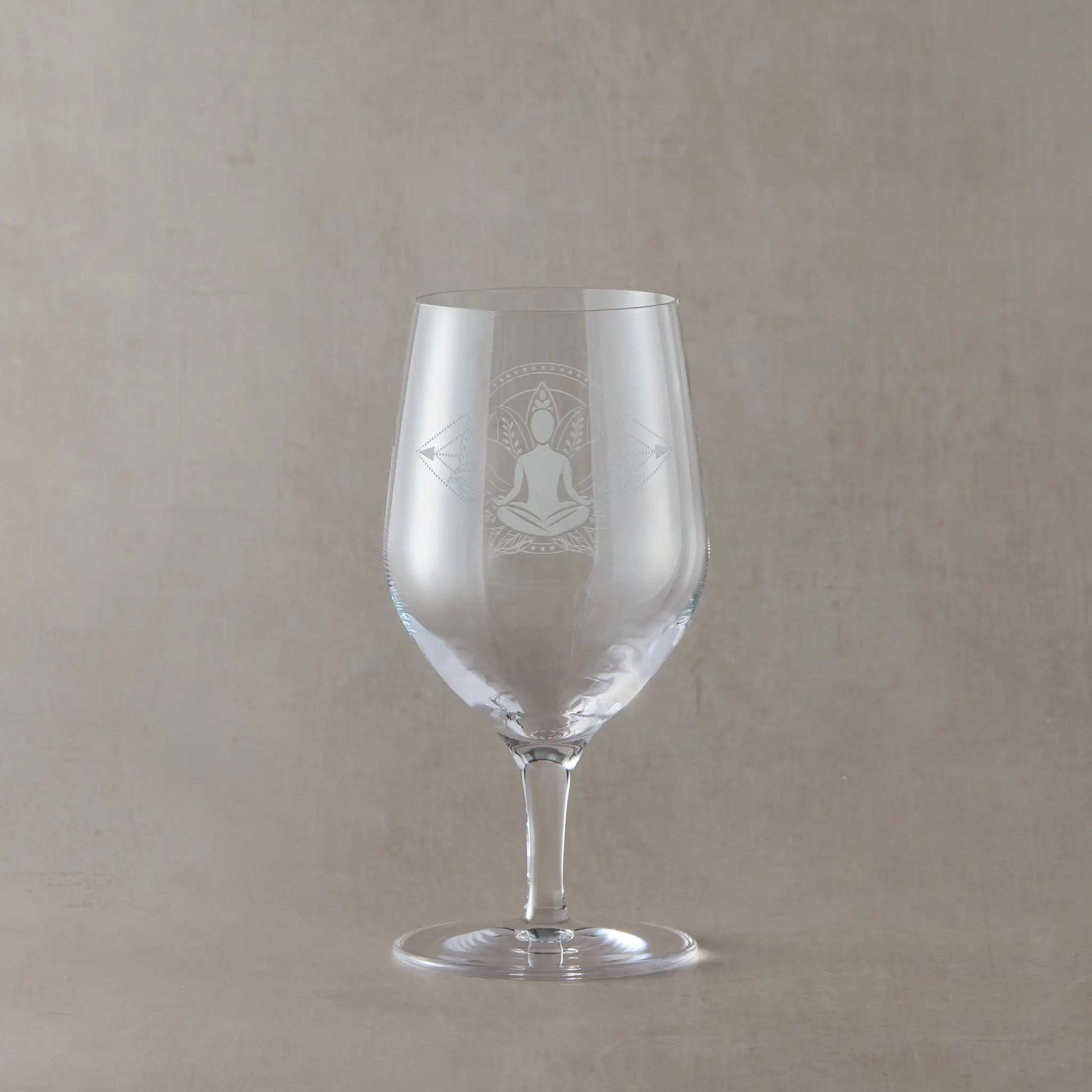 Mineral water glass engraved with a lotus flower and male yoga pose photographed on a beige background