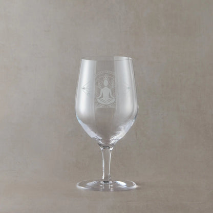 Mineral water glass engraved with a lotus flower and male yoga pose photographed on a beige background
