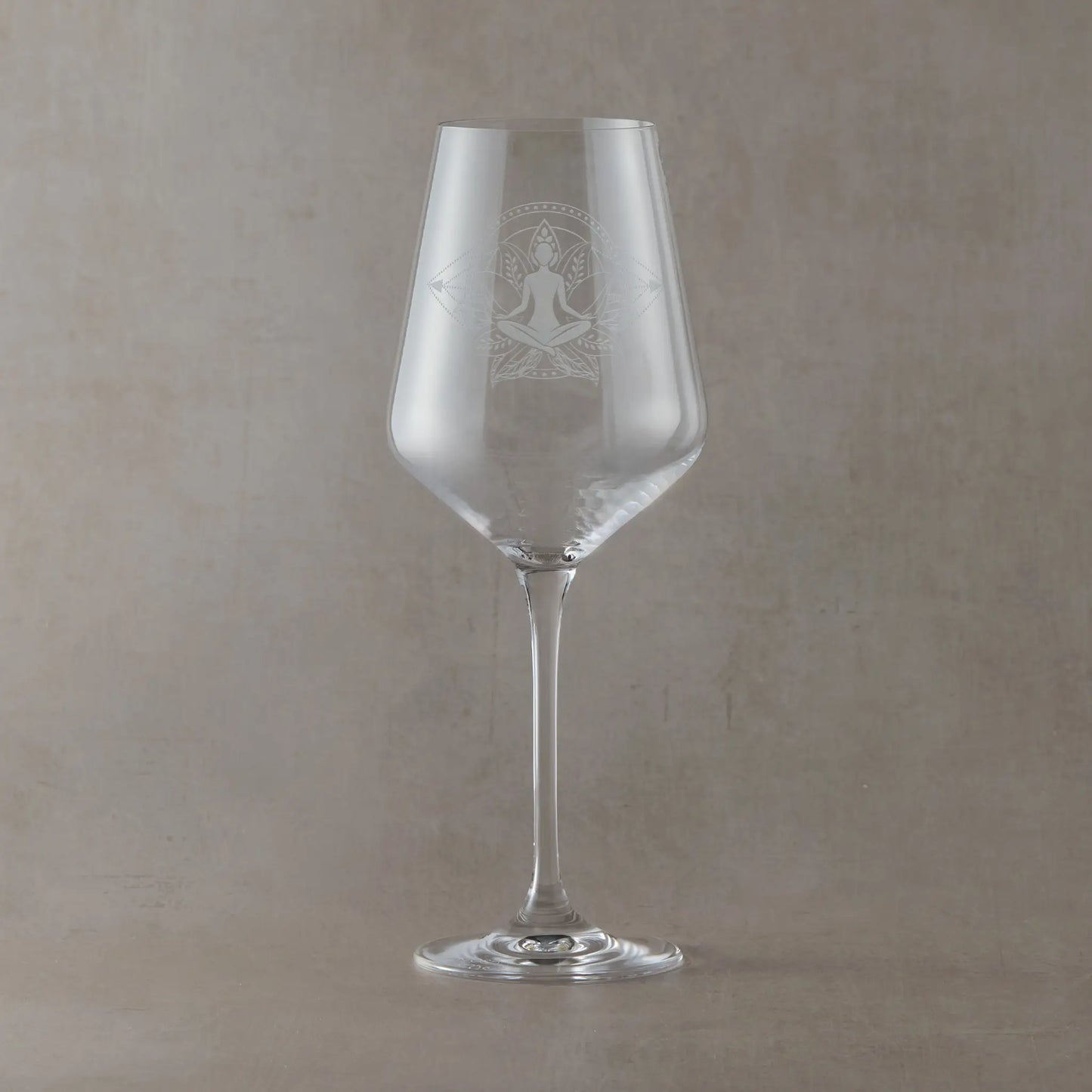 Hand-engraved Atelier wine glass featuring a seated yoga figure in a lotus pose within a lotus flower design, sandblasted onto clear glass against a neutral beige studio background