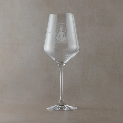 Hand-engraved Atelier wine glass featuring a seated yoga figure in lotus pose within a lotus flower design, sandblasted onto clear glass against a neutral beige studio background