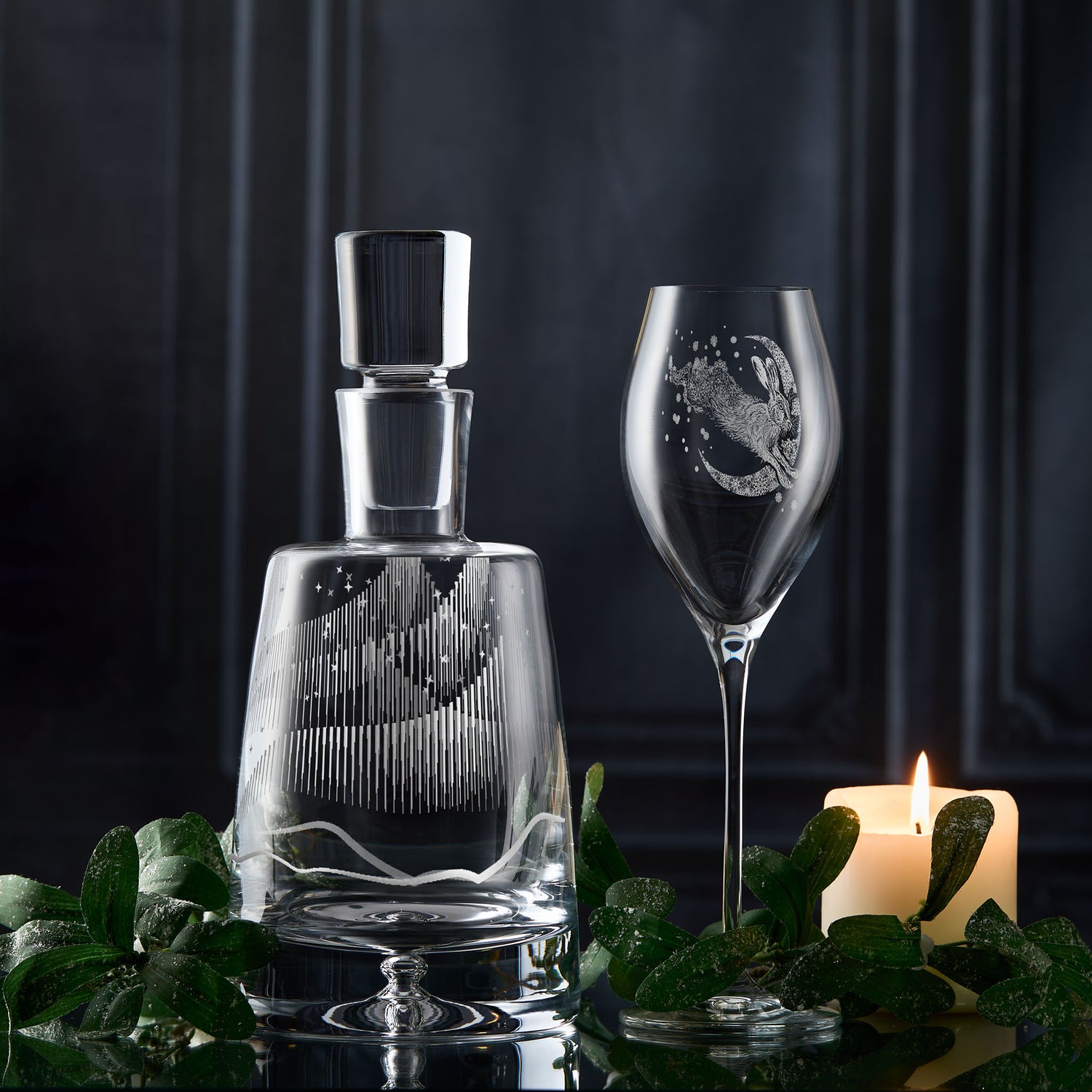 Northern lights glass decanter and wine glass with engraved moon and stars design on a dark background