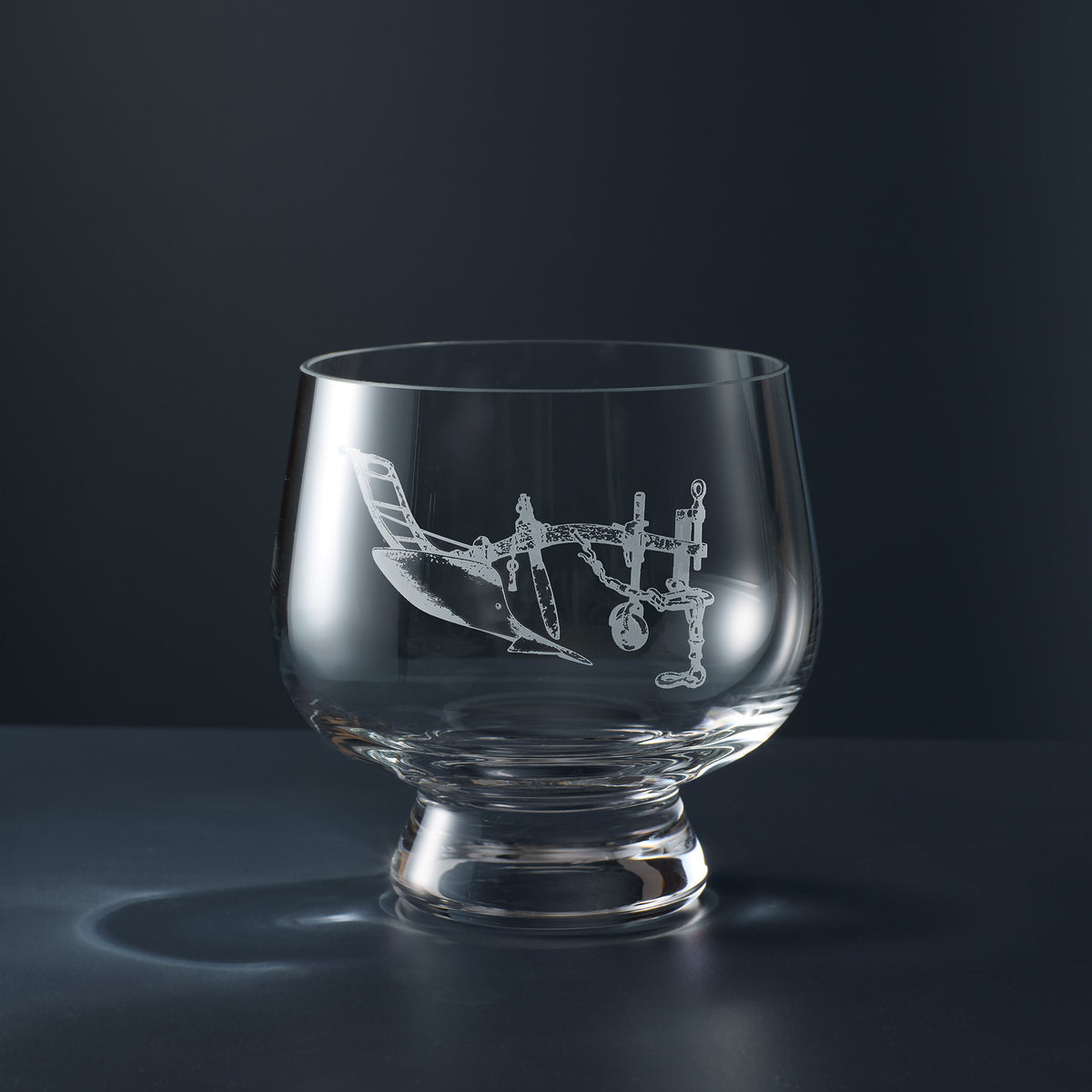 A clear glass rose bowl engraved with an illustration of a vintage plough.