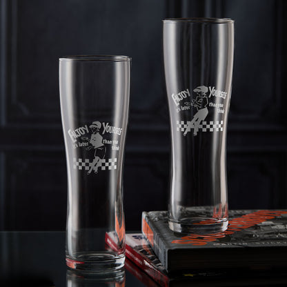Two engraved Beat Girl pint glasses with “Enjoy Yourself” text and checkerboard design.