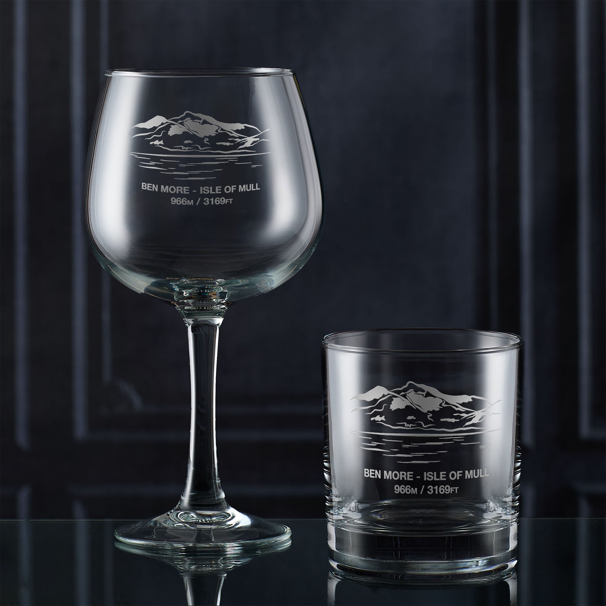 Gin glass and whisky tumbler engraved with Ben More, photographed on a dark background