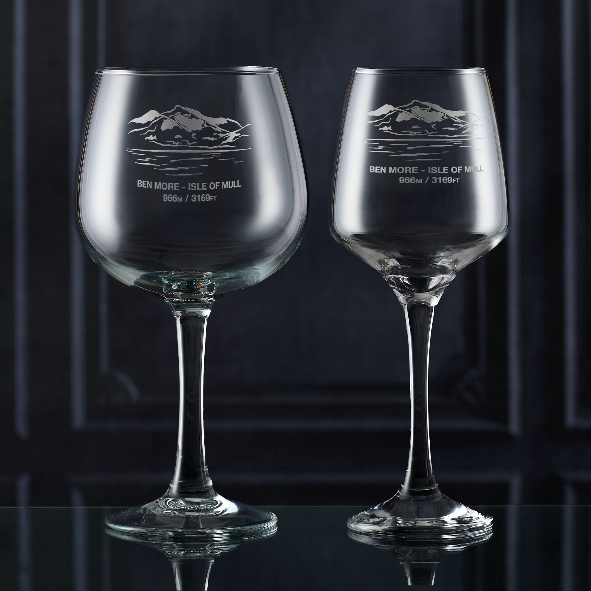 Gin glass and wine glass engraved with Ben More, photographed on a dark background