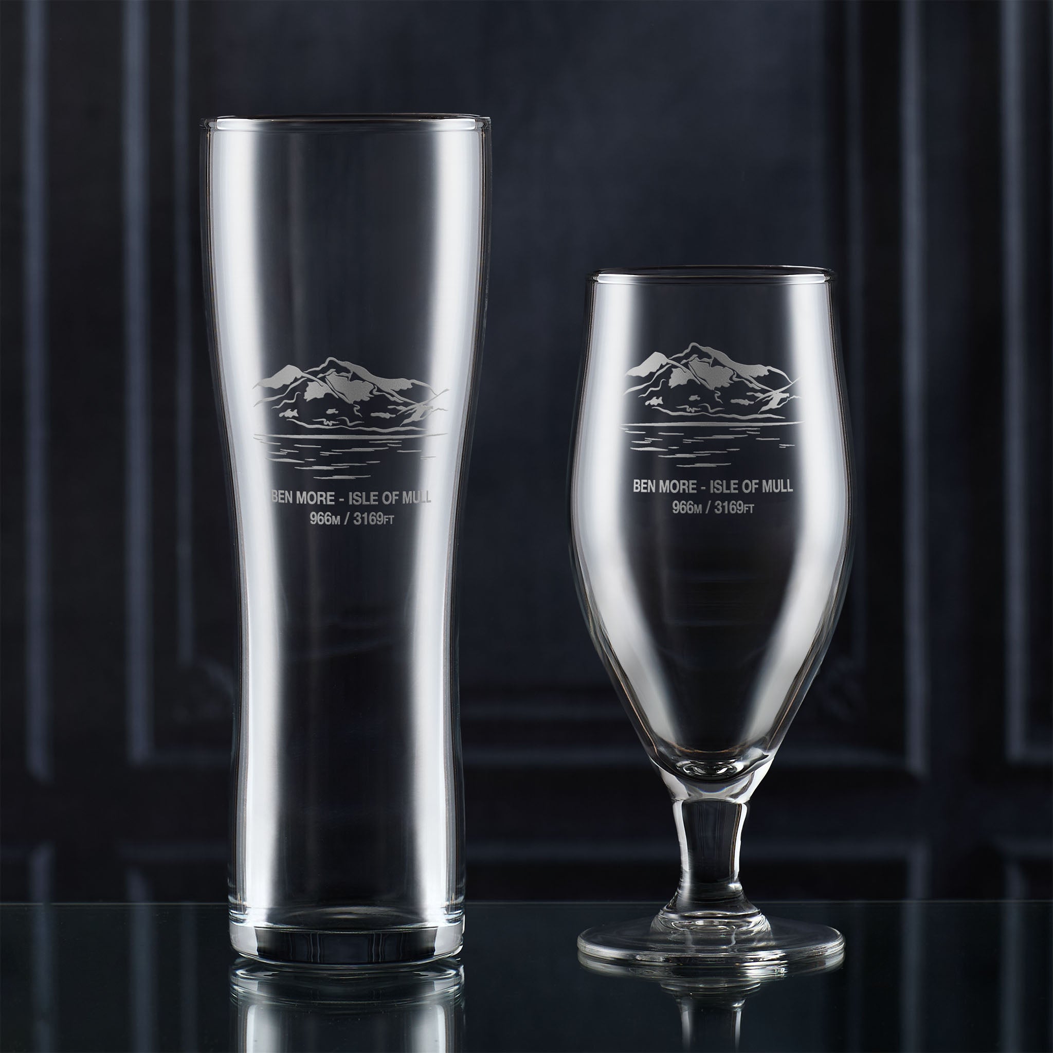 Two beer glasses with engraved Ben More mountain design on a dark background