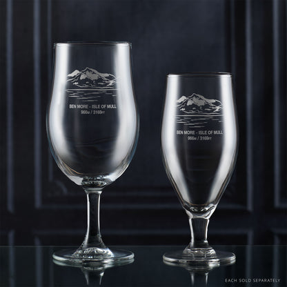 Two stemmed beer glasses with engraved mountain design on a dark background