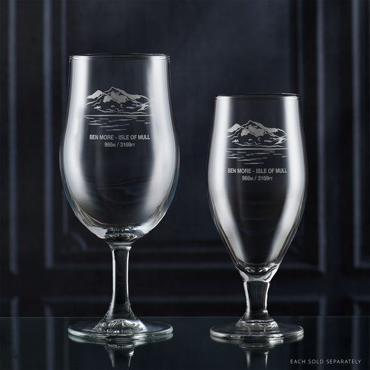 Two stemmed beer glasses with engraved mountain design on a dark background