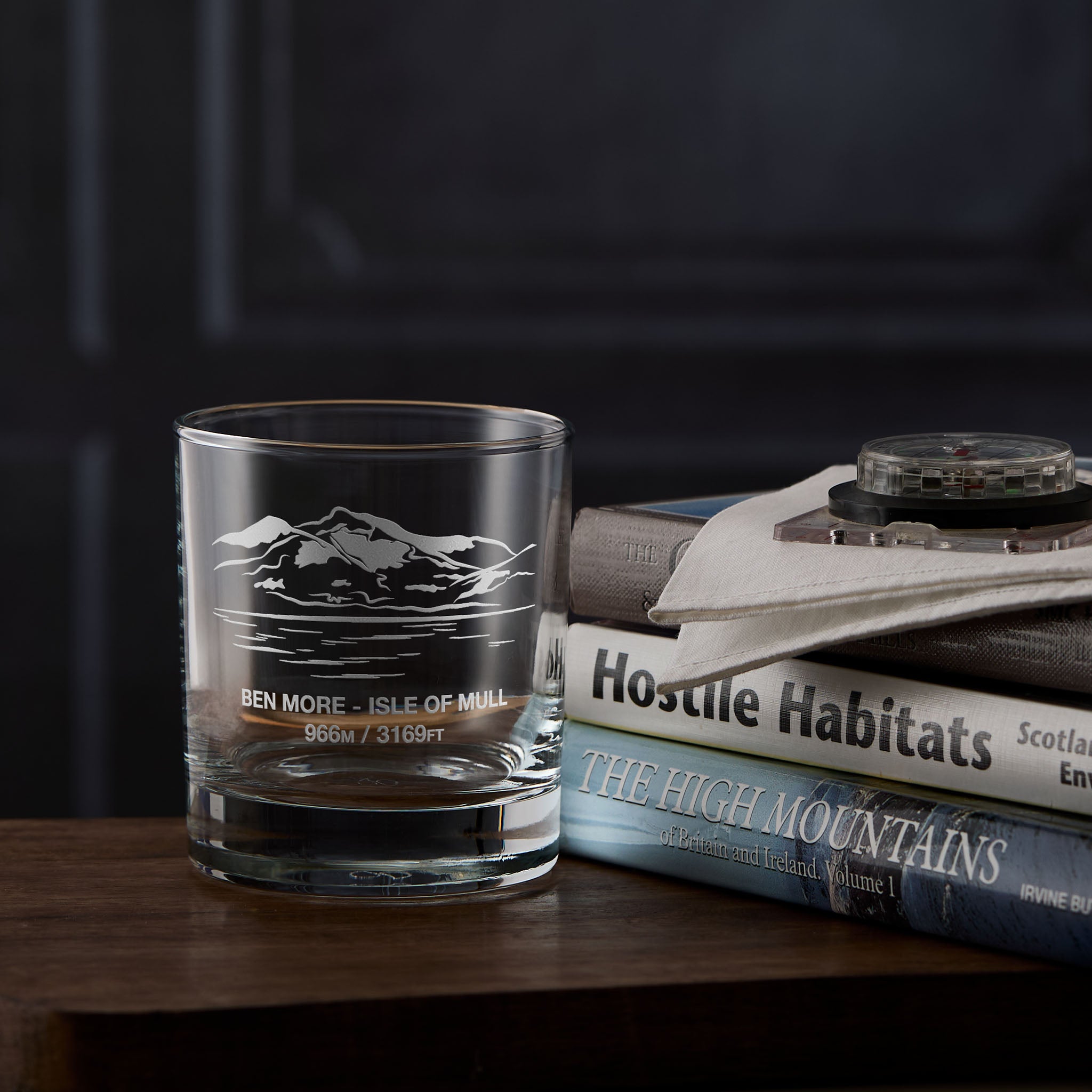 Clear whisky glass engraved with the scottish mountain Ben More placed next to  a stack of books