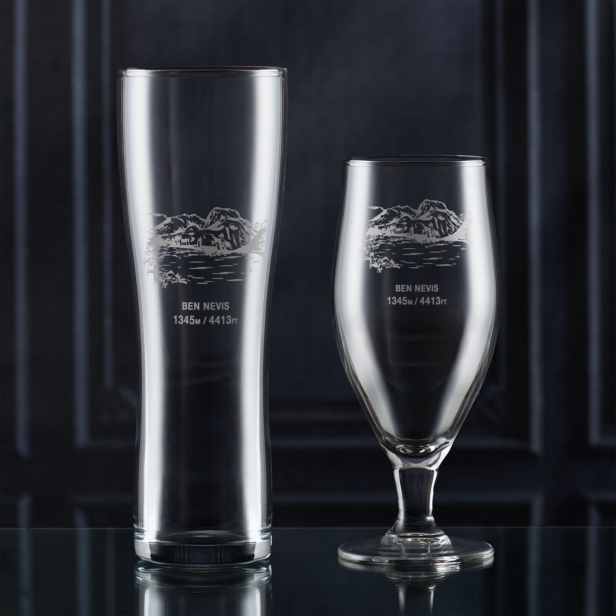Pint glass and stemmed beer glass engraved with Ben Nevis, photographed on a dark background
