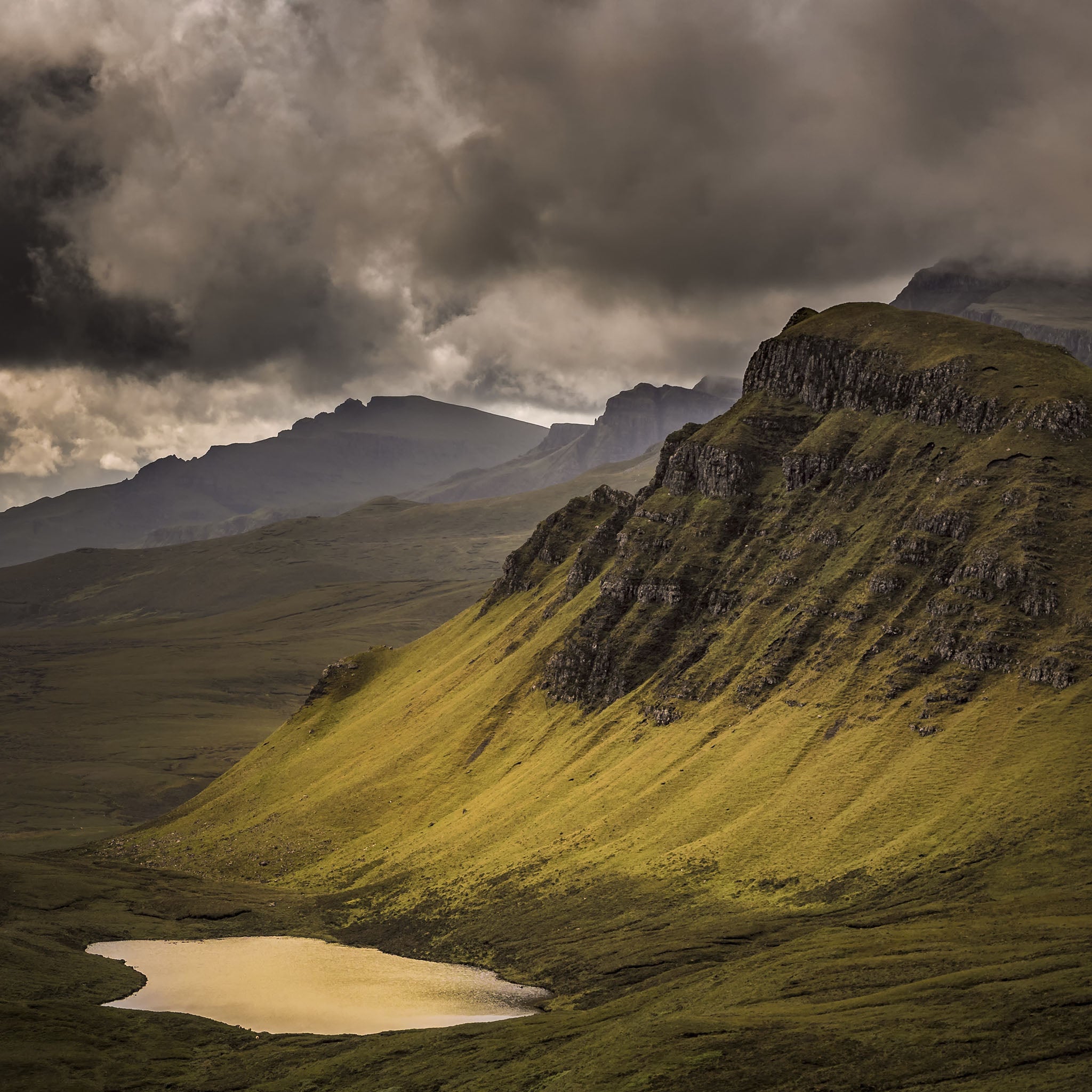 Green mountain landscape with a lake and dark clouds in the sky