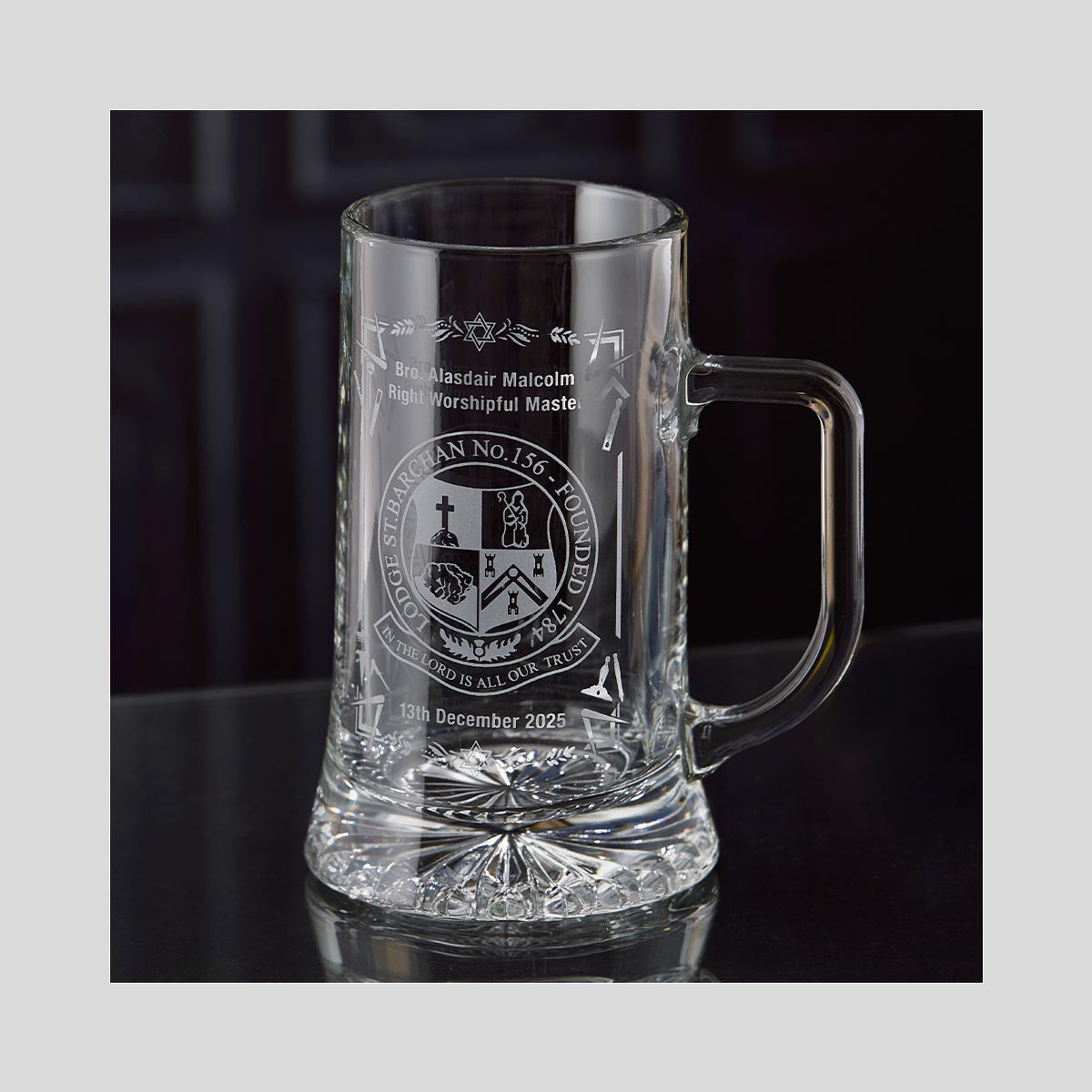 Clear glass beer tankard with engraved masonic design on a dark background
