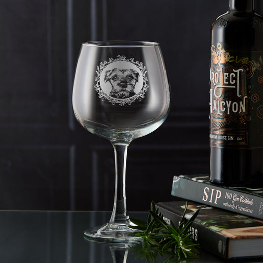 Hand-engraved Border Terrier gin glass displayed in front of dark wooden panelling, showing a straight-on portrait with leafy garland design by Just The Ticket.