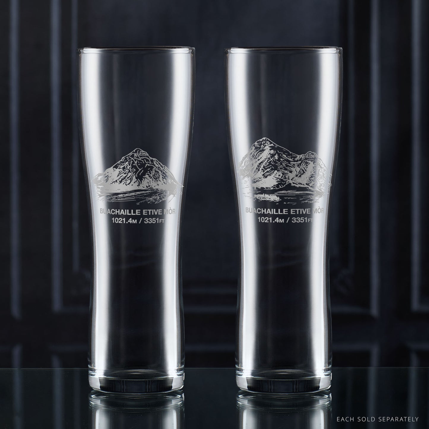 Two clear pint glasses with mountain etching on a dark background