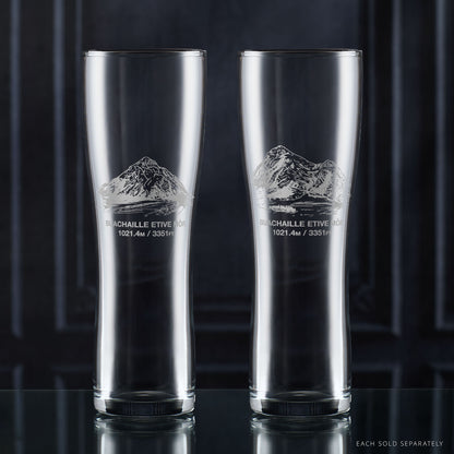 Two clear pint glasses with mountain etching on a dark background