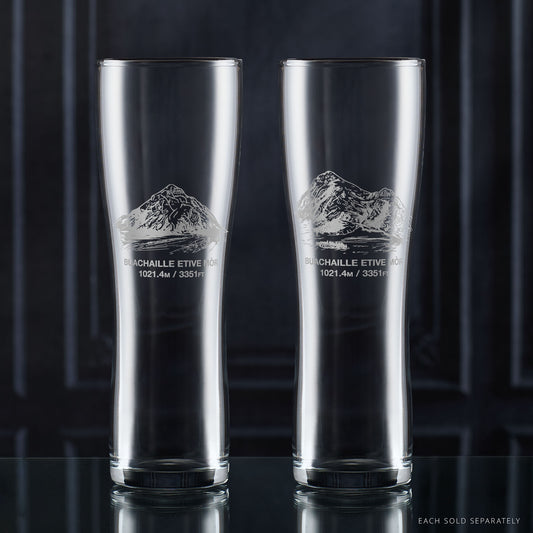 Two clear pint glasses with mountain etching on a dark background