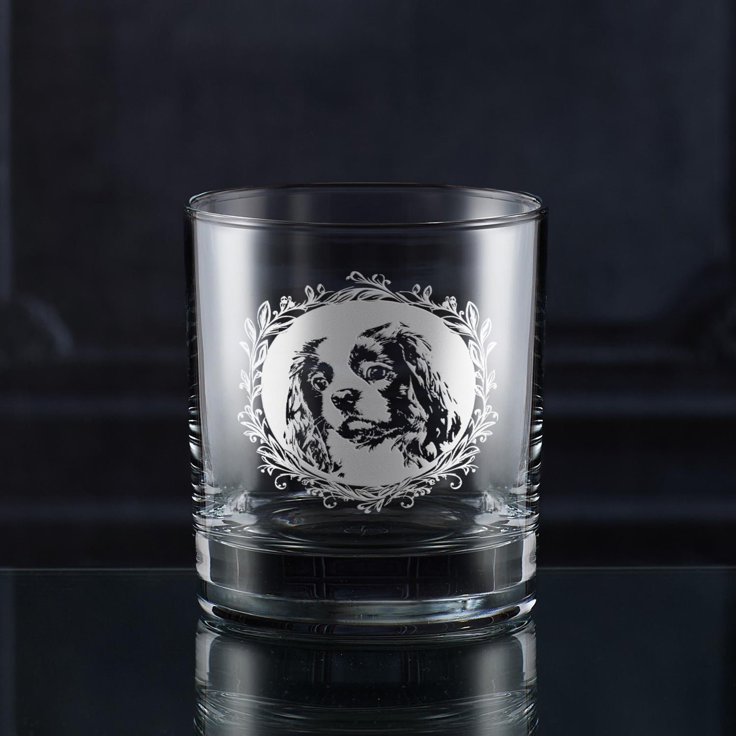Hand-engraved Cavalier King Charles Spaniel whisky glass displayed against dark wood panelling, featuring leafy garland dog portrait design by Just The Ticket.