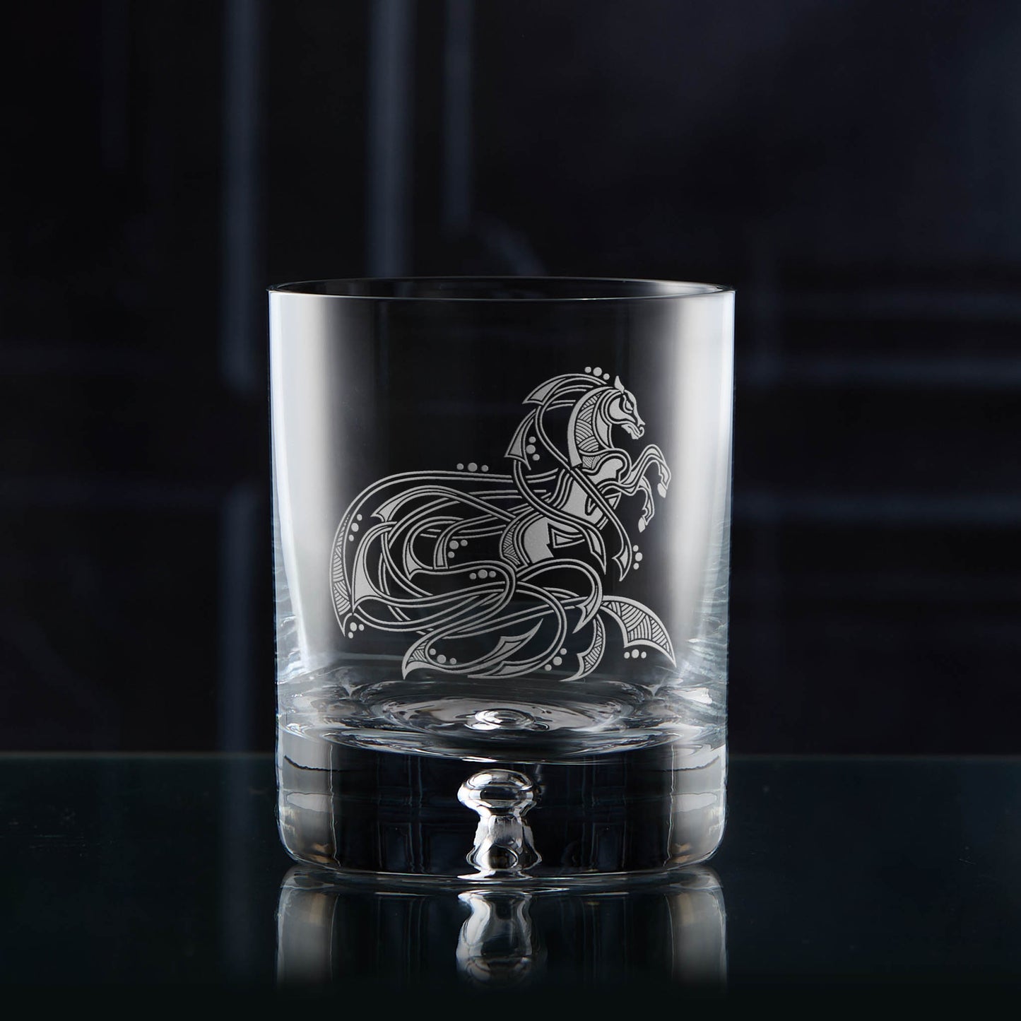 Clear glass tumbler with intricate horse design on a dark background