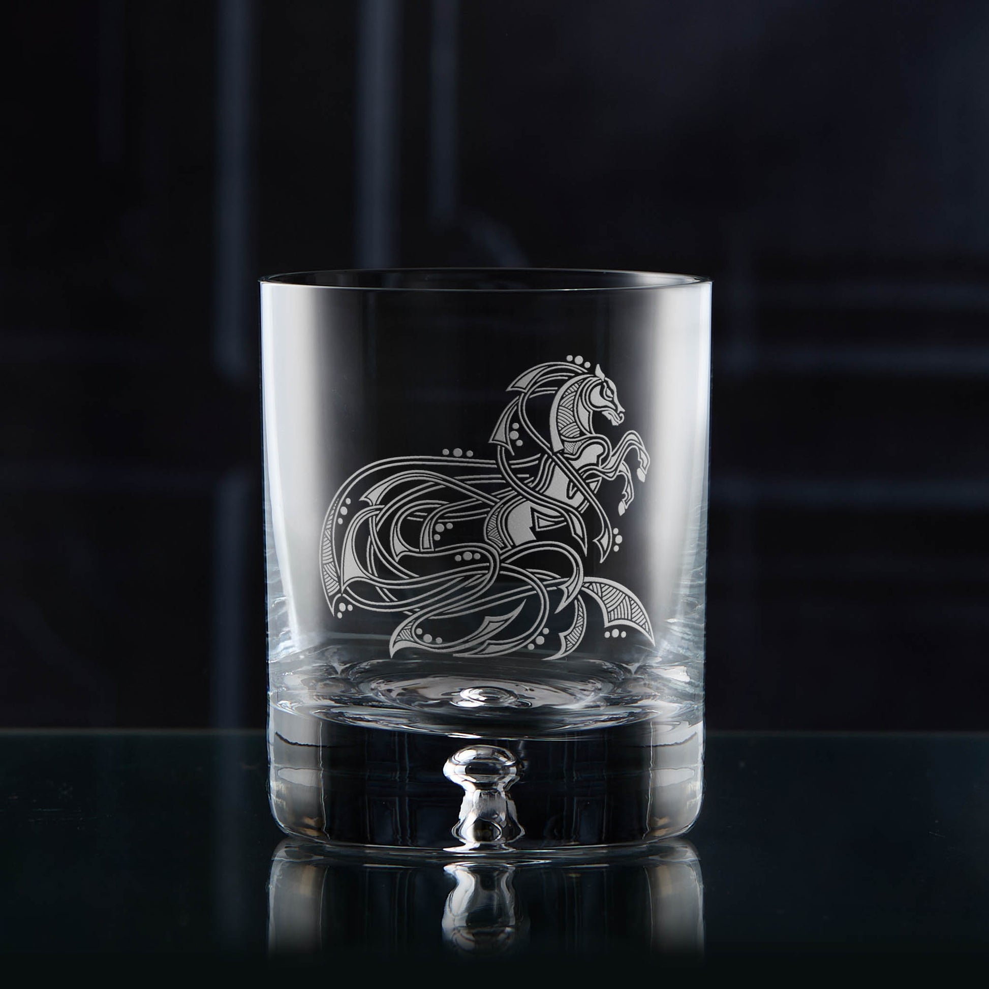 Clear glass tumbler with intricate horse design on a dark background
