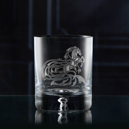 Clear glass tumbler with intricate horse design on a dark background