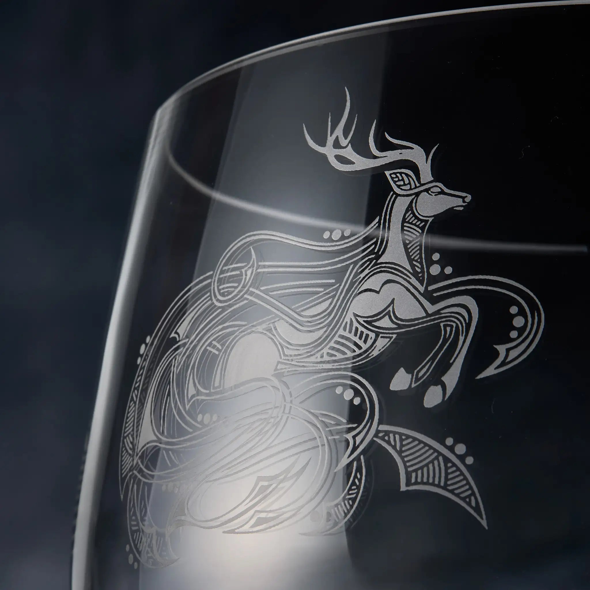 Glass with an engraved deer design on a dark background