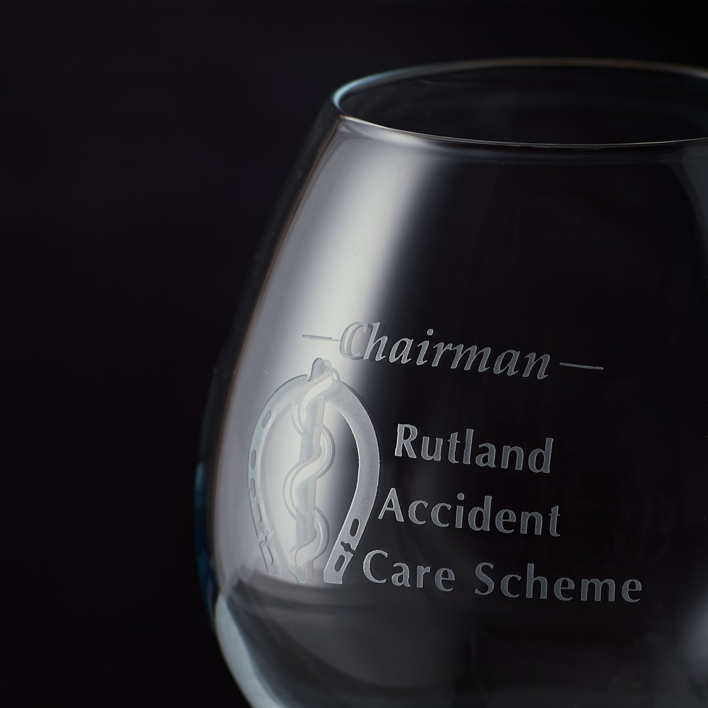 Close up of sandblast engraving on a brandy glass with engraved text and business logo on a black background