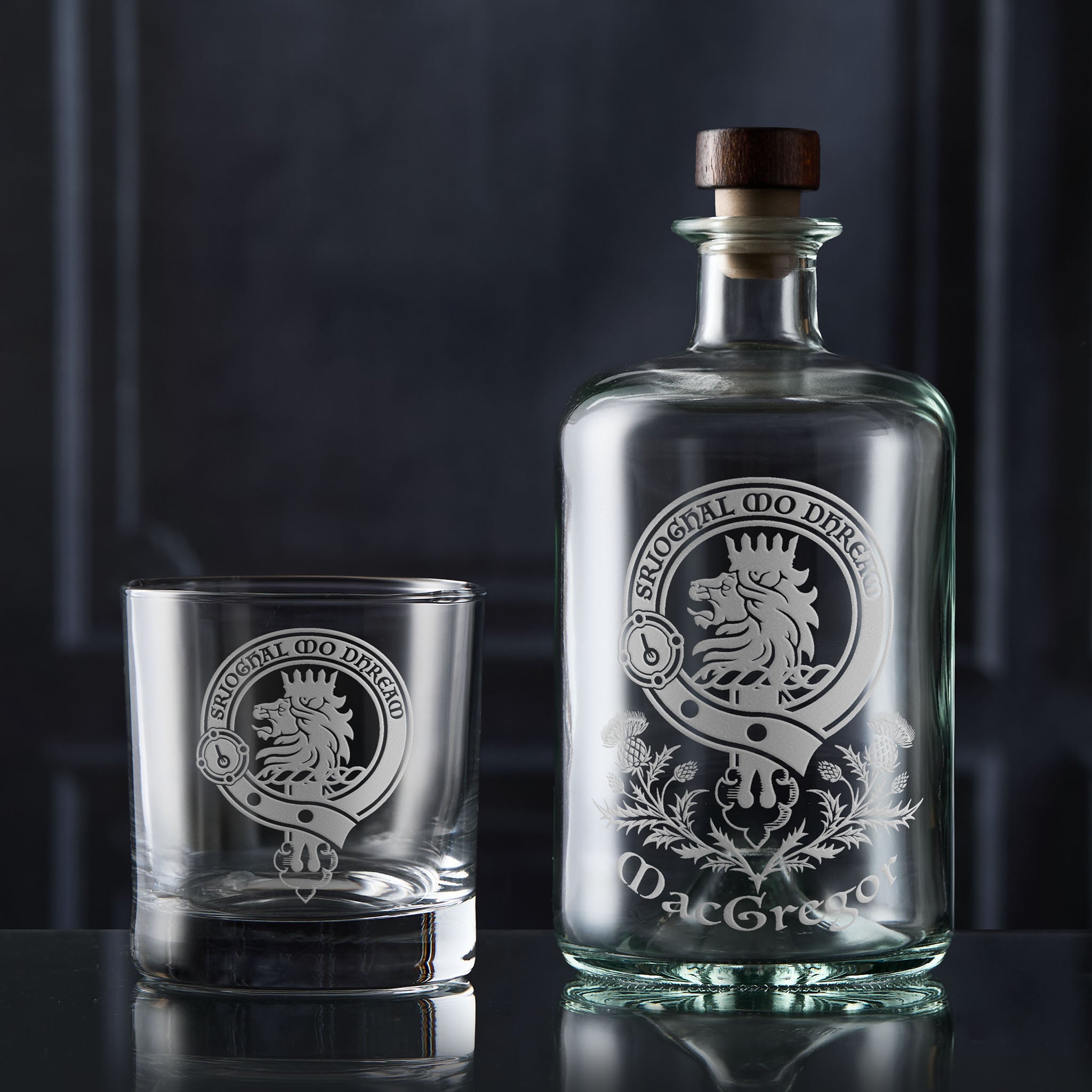 Glass decanter and tumbler with MacGregor clan crest on a dark background