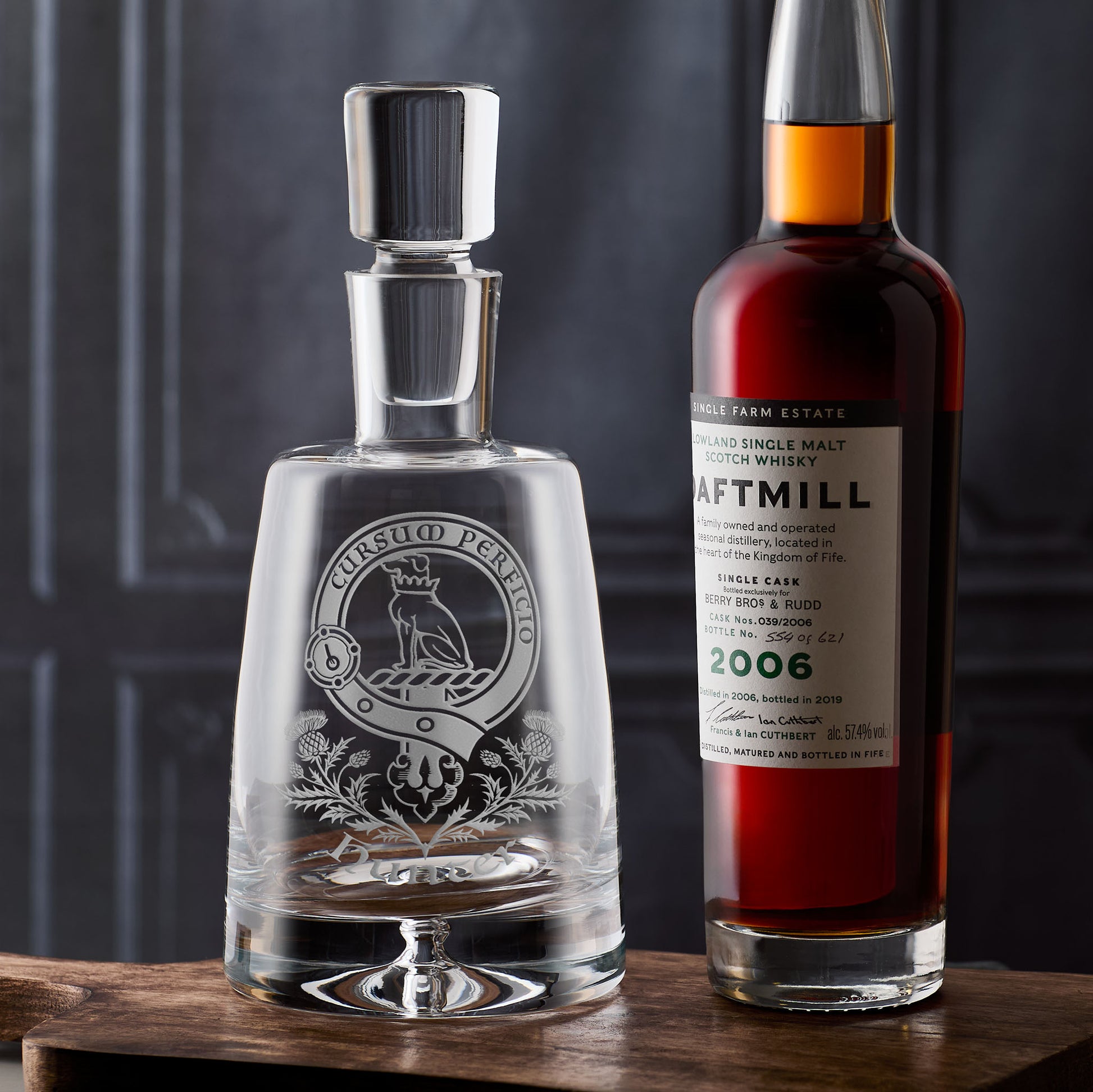 Atelier Edition decanter engraved with traditional Scottish clan crest, strap-and-buckle motto, thistles, and surname, shown on a dark background