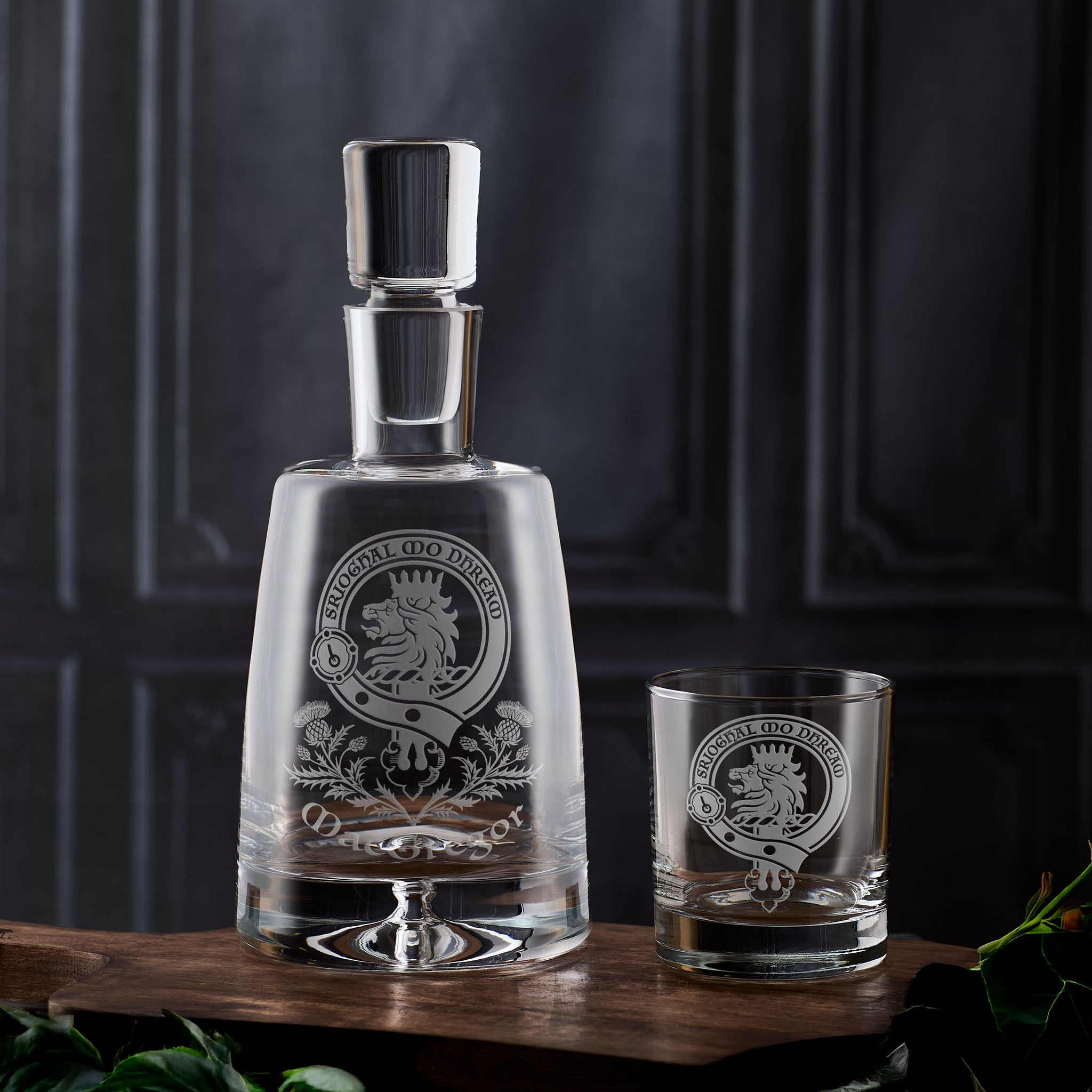 Scottish Clan Crest Glass decanter and tumbler with engraved design on a wooden surface against a dark background