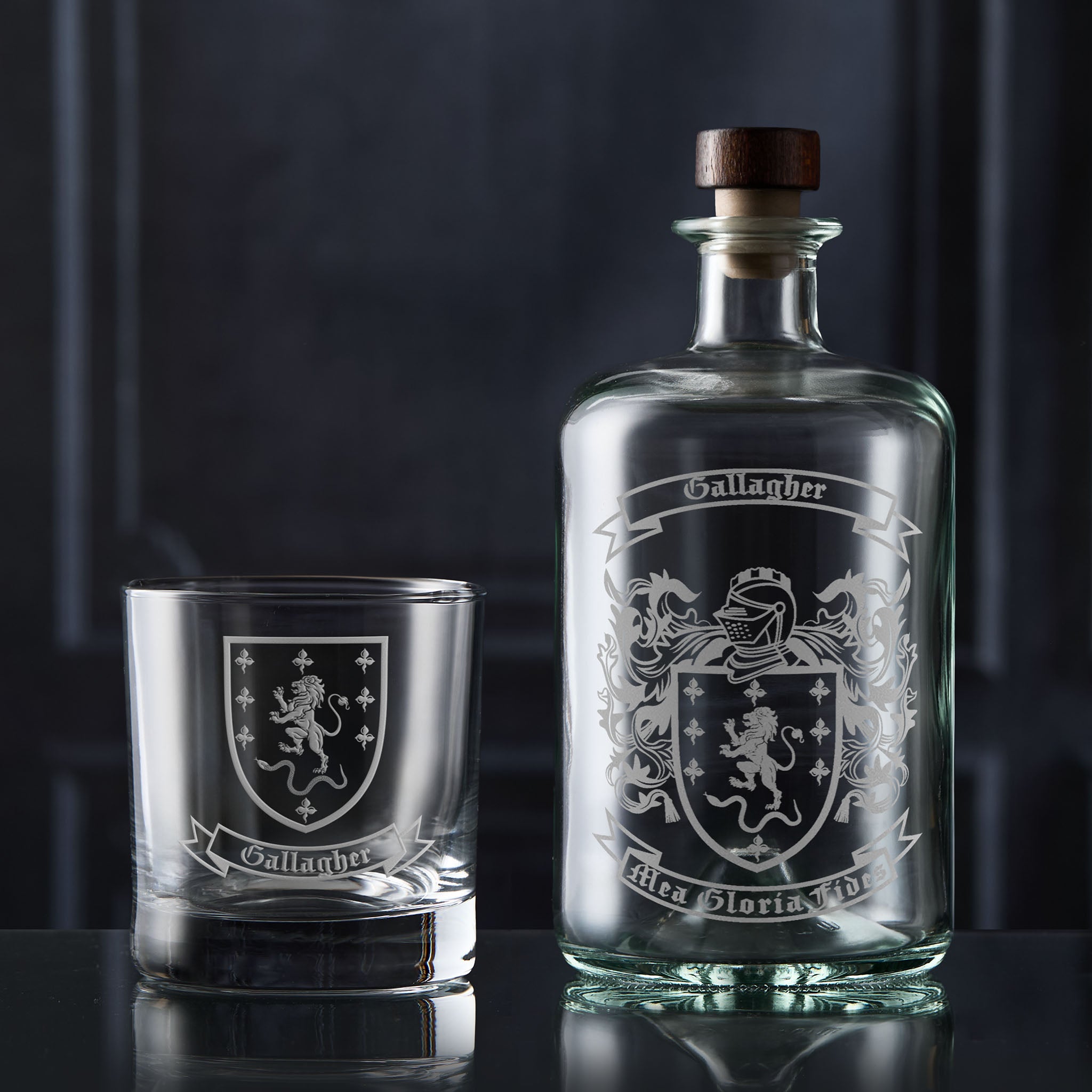 Glass decanter and tumbler with engraved family crest and heraldic Coat of Arms on a dark background