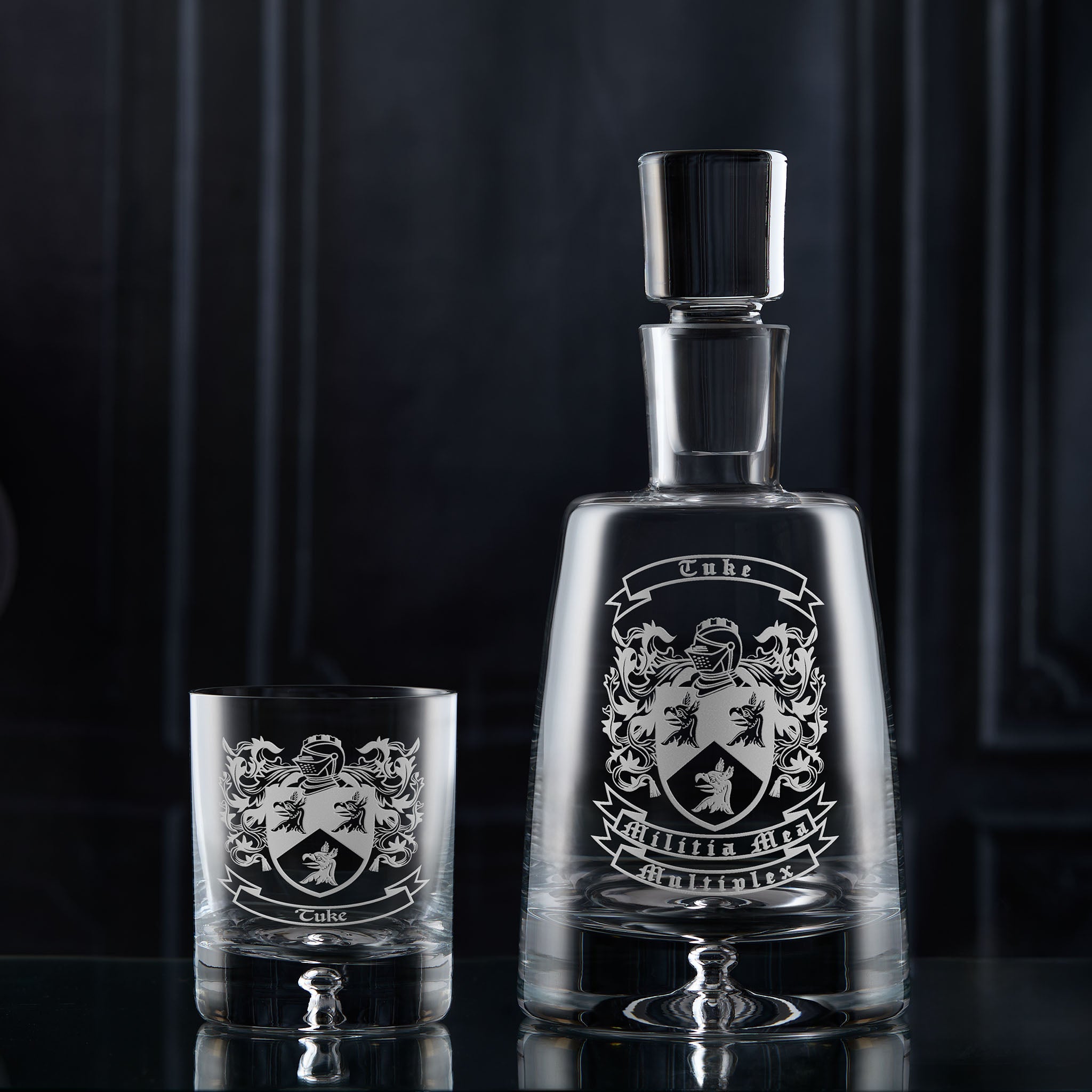 Heraldic decanter and whisky glass with engraved family crest on a dark background