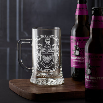 Glass tankard with engraved coat of arms heraldry design and two bottles of beer on a wooden board.