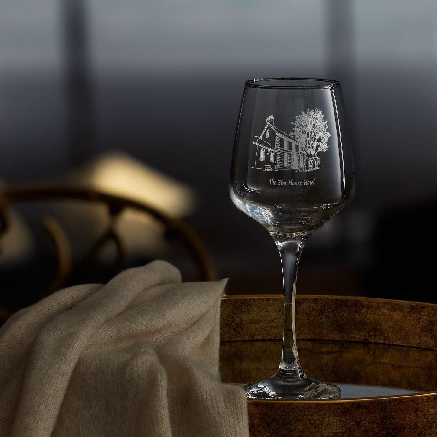 Wine glass with engraved hotel design on a wooden surface with a blurred background
