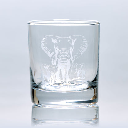 Engraved whisky glass featuring a mother elephant and her two calves, photographed on a white background to show glass clarity and design detail.