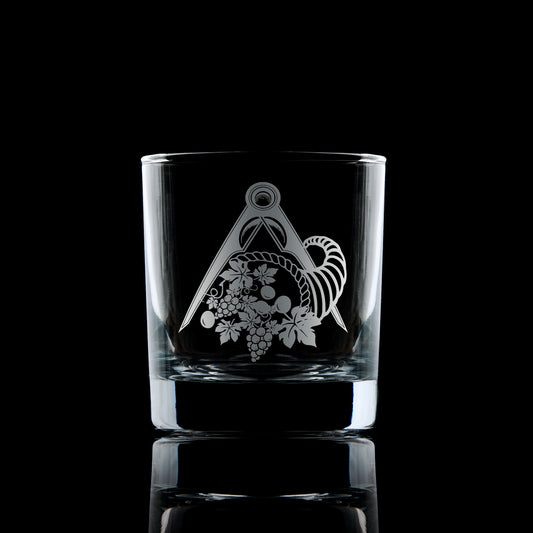 Engraved whisky glass with cornucopia symbol for Masonic Stewards, photographed on a dark textured backdrop