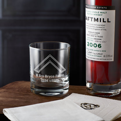 Masonic whiskey glass engraved with the worshipful master design and personalised inscription next to a bottle of Daftmill whisky on a wooden surface.