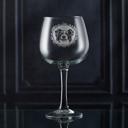 Hand-engraved Border Collie gin glass shown in front of a dark panelled wall, featuring a leafy garland and detailed Collie portrait design by Just The Ticket.