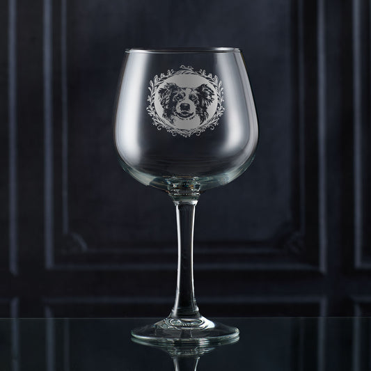 Hand-engraved Border Collie gin glass shown in front of a dark panelled wall, featuring a leafy garland and detailed Collie portrait design by Just The Ticket.