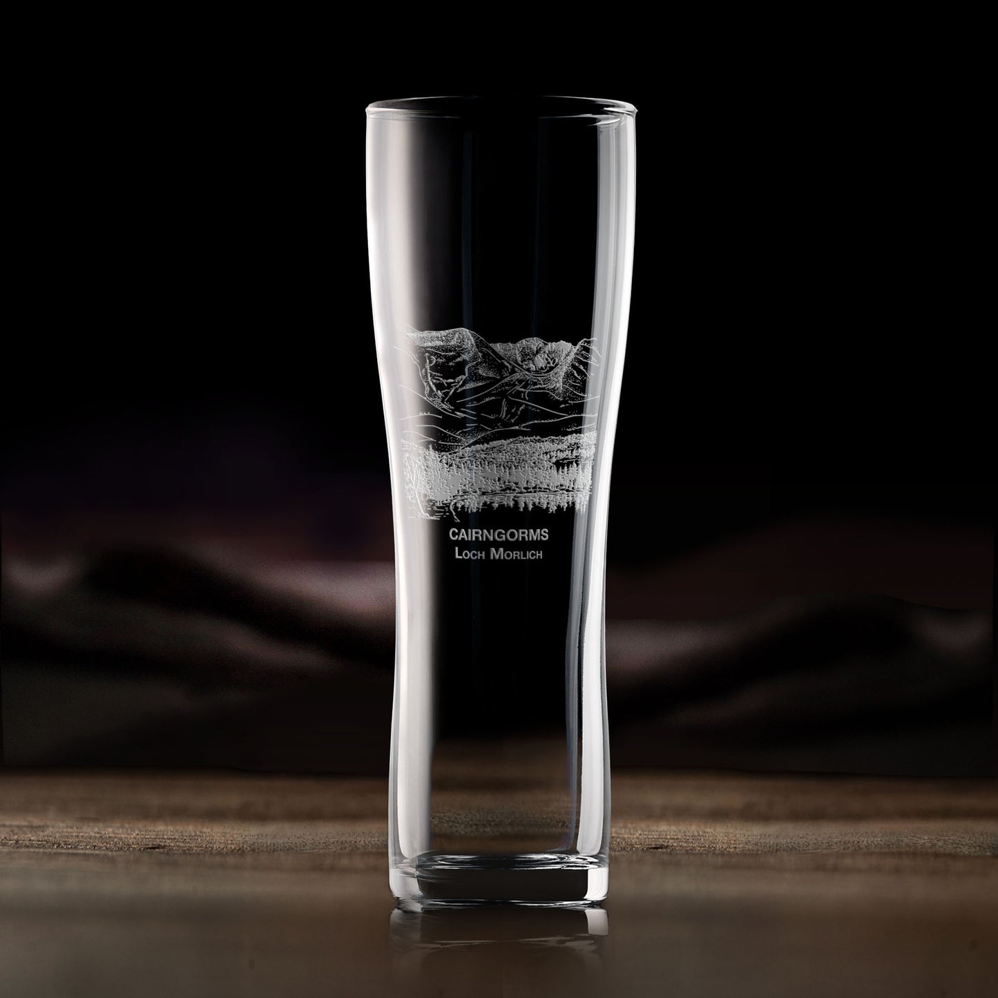 Engraved pint glass with Cairngorms and Loch Morlich landscape, shown on dark background to highlight engraving