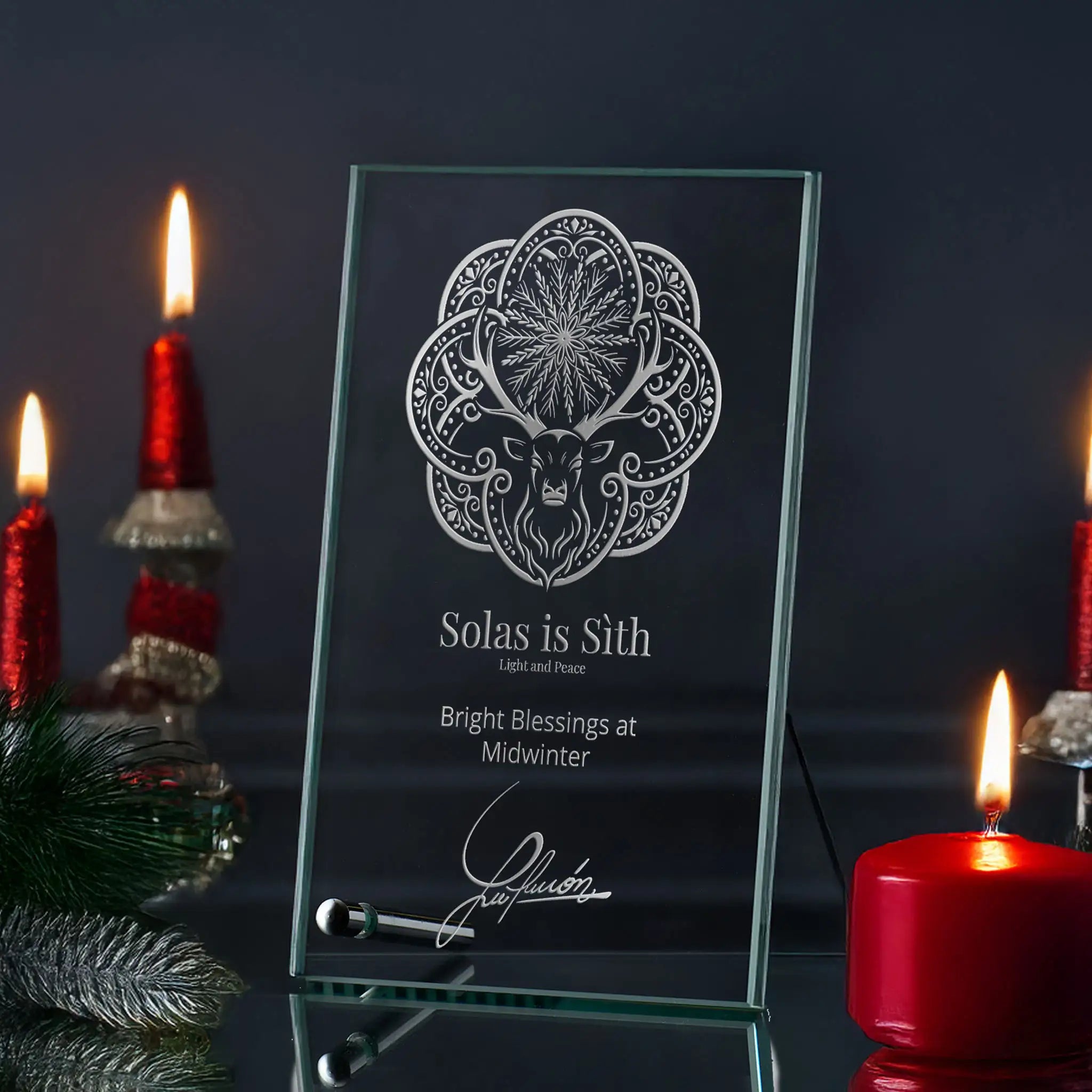 Glass plaque with engraved christmas design and text, surrounded by candles on a dark background