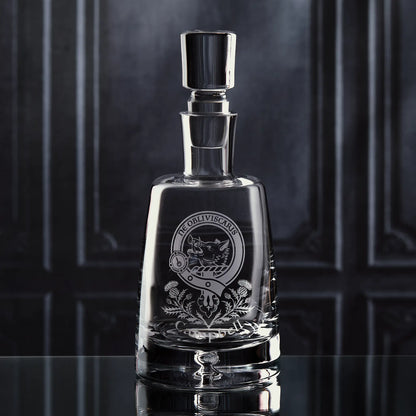 Handmade glass decanter engraved with personalised clan crest and thistle motif, shown on dark background to highlight shape and craftsmanship
