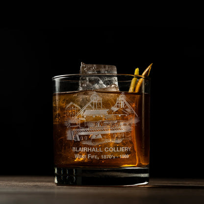 Glass of whiskey with ice featuring an engraved coal mine design on a dark background