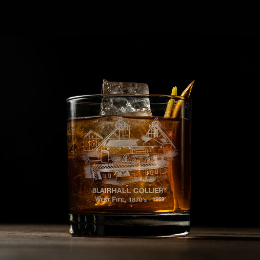 Glass of whiskey with ice featuring an engraved coal mine design on a dark background