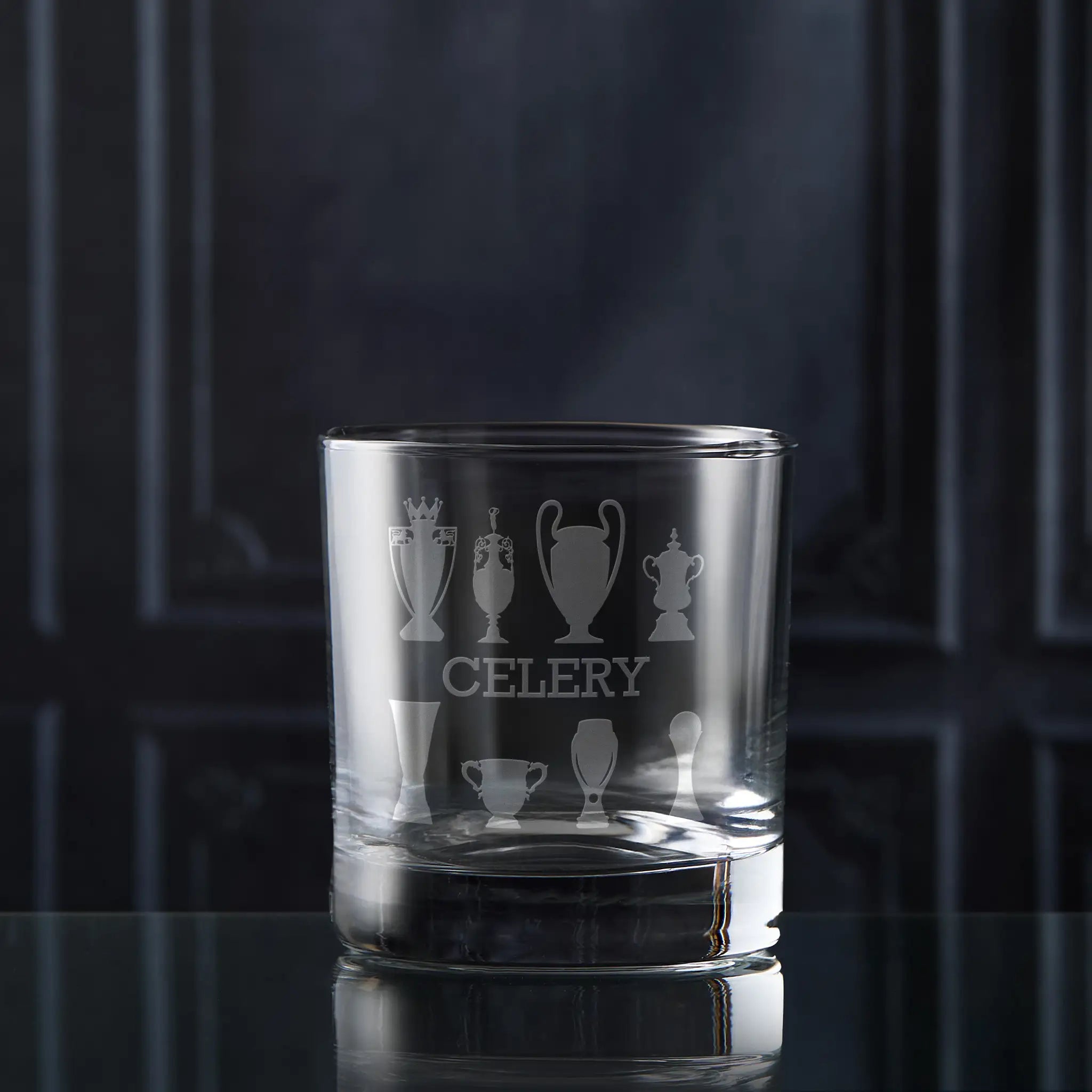 Clear glass tumbler with engraved football trophy designs and 'CELERY' text on a dark background