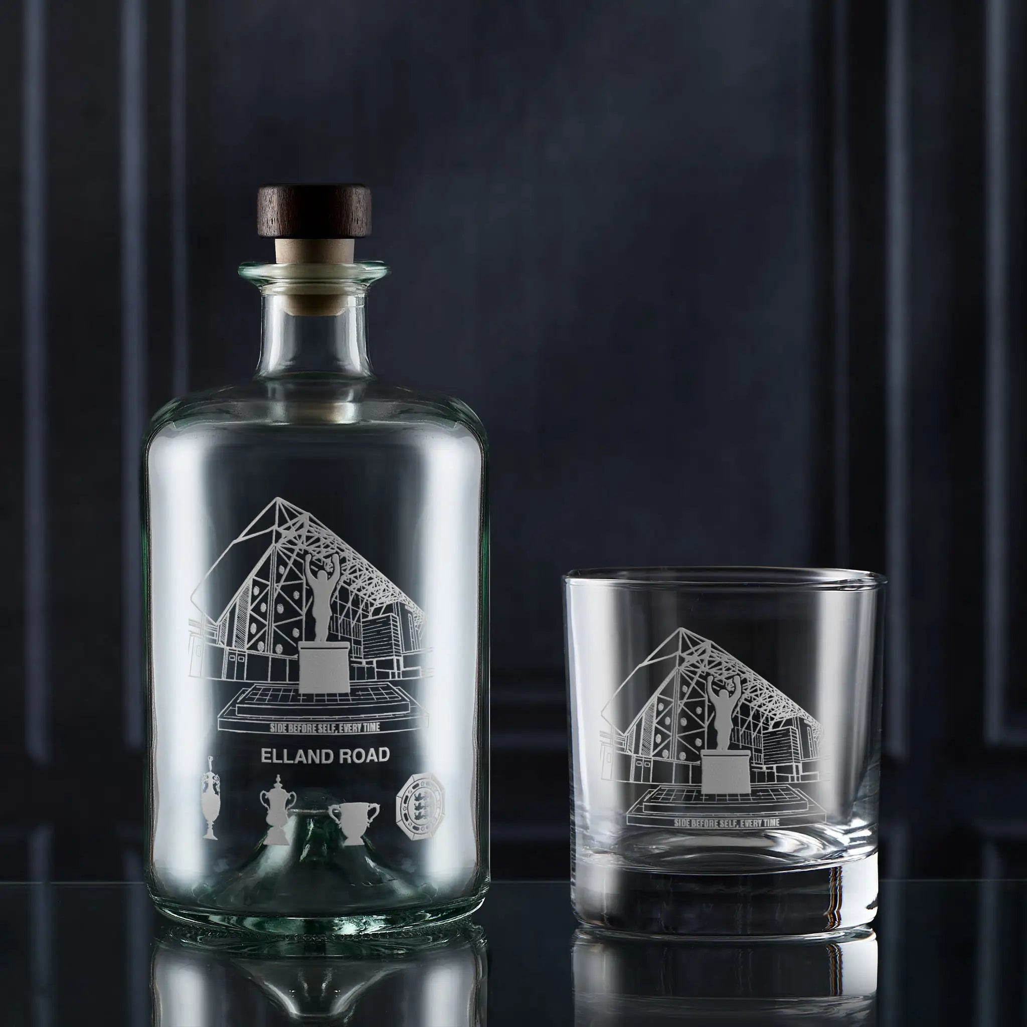 Glass bottle and glass with engraved football stadium design on a dark background