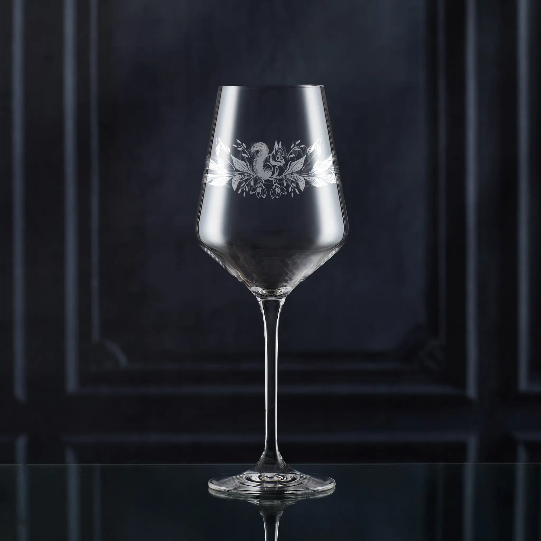 Clear wine glass with decorative snowdrop and squrrel etching on a dark background