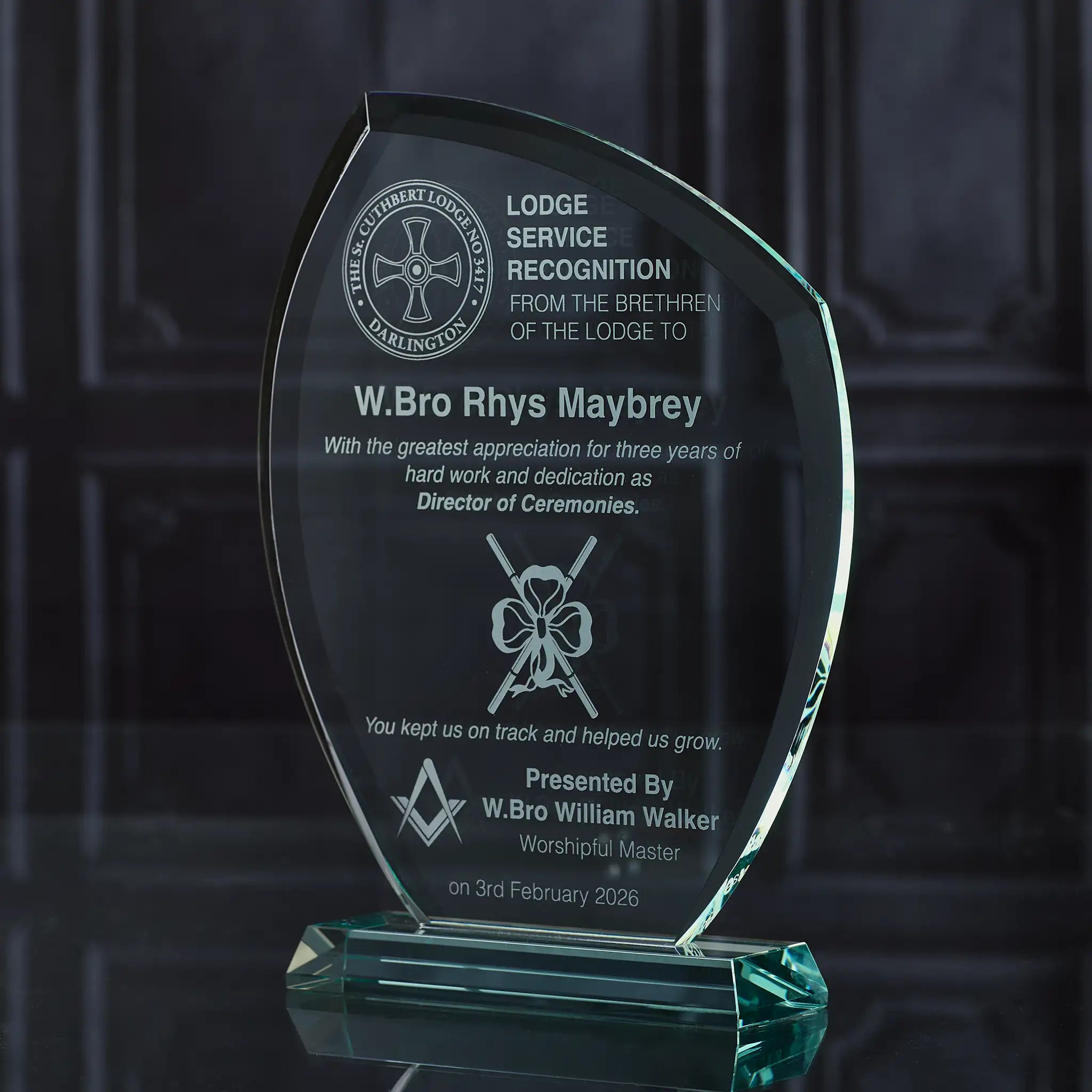 Glass award with engraved text and Masonic symbols on a dark background