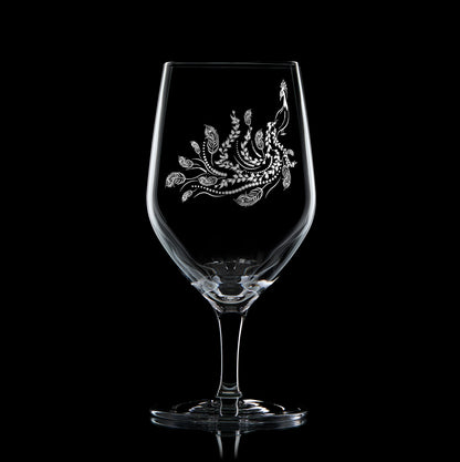 Engraved mineral water glass featuring peacock design with trailing feathers, shown on a black background